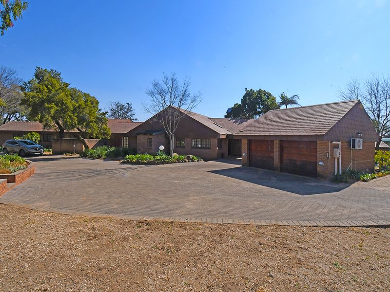 Front exterior view of a single-story brick house featuring a large paved driveway, double garage, and established garden surroundings.