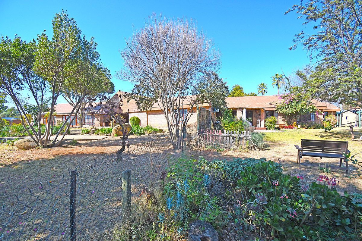 A spacious rear garden area featuring established trees, a lawn, and a view of the single-story brick house exterior.