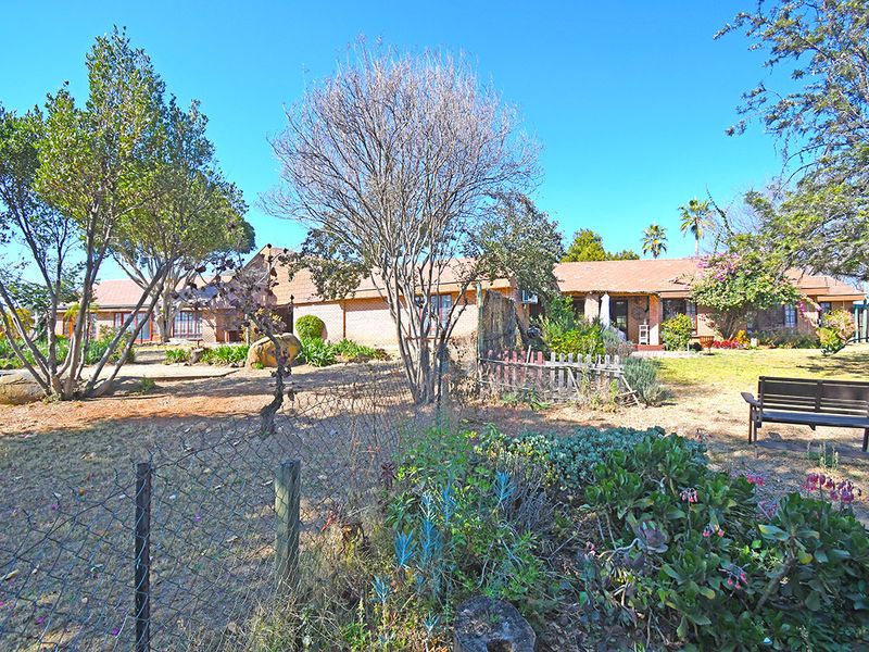 A spacious rear garden area featuring established trees, a lawn, and a view of the single-story brick house exterior.