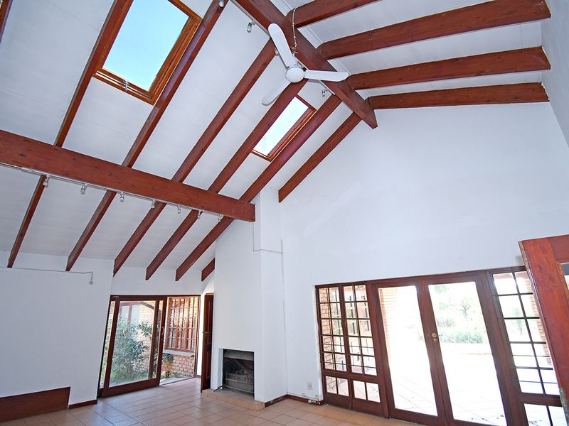 Spacious living area featuring high vaulted ceilings with exposed timber beams, skylights, a built-in fireplace, and large glass doors opening to the exterior.