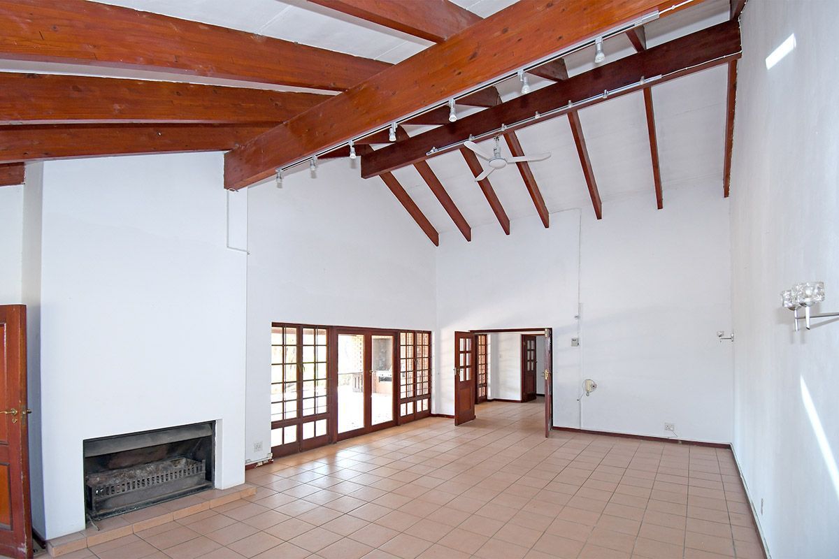 Spacious living area featuring high vaulted ceilings with exposed timber beams, tiled flooring, and a built-in fireplace with direct access to the patio.