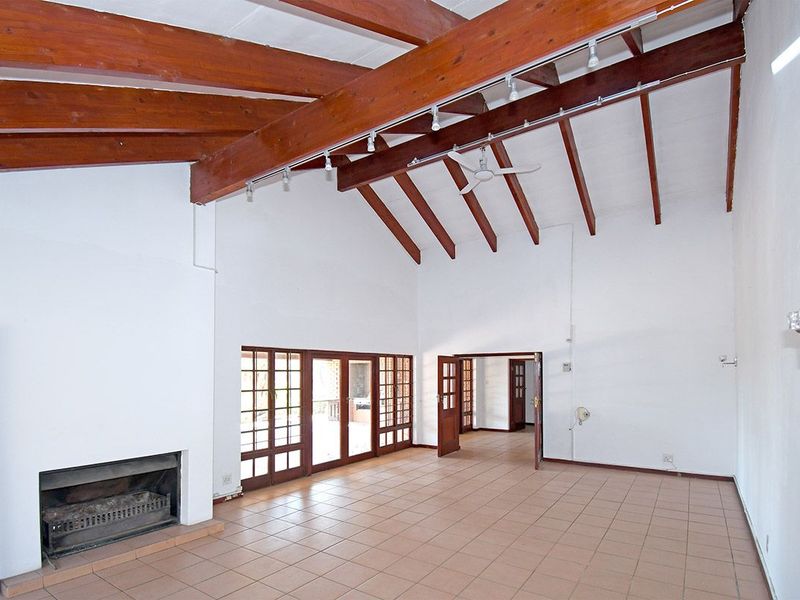 Spacious living area featuring high vaulted ceilings with exposed timber beams, tiled flooring, and a built-in fireplace with direct access to the patio.