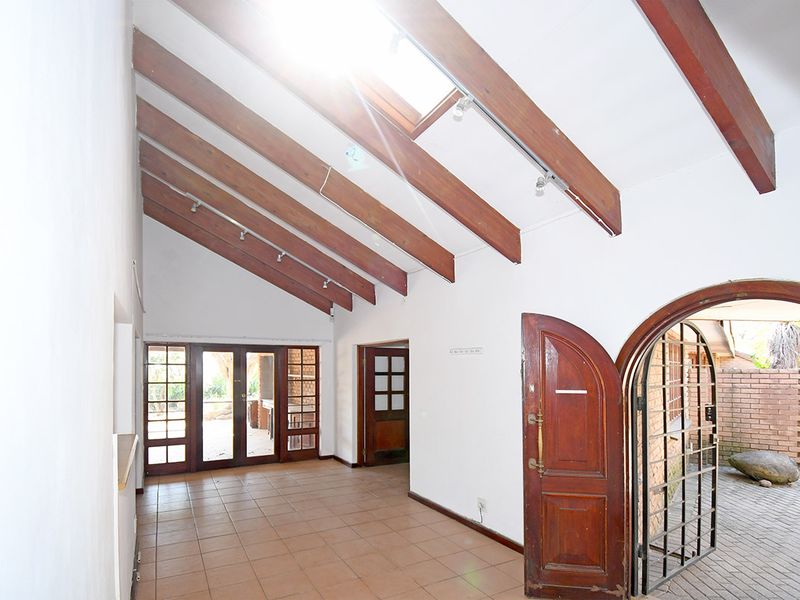 Spacious entrance hall featuring vaulted ceilings with exposed timber beams, skylight, tiled flooring, and direct access to the outdoor patio area.