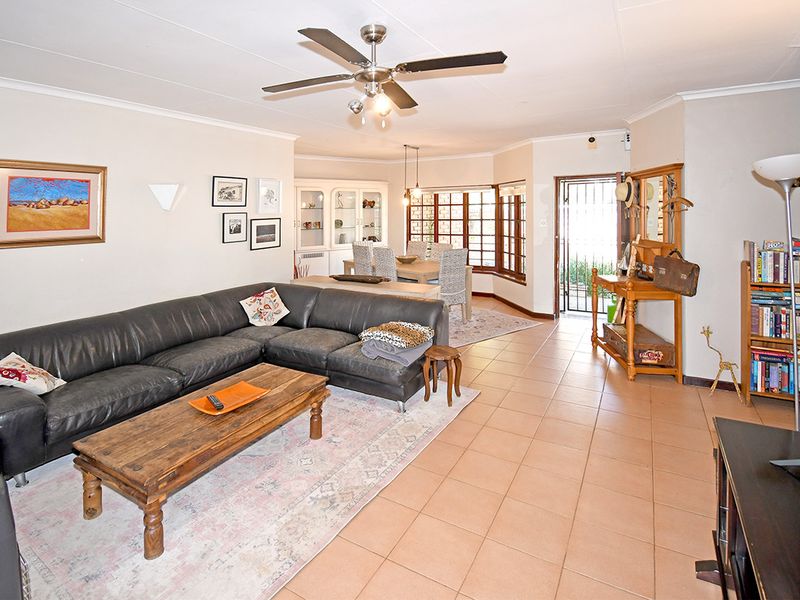 Spacious open-plan living and dining area featuring tiled flooring, a ceiling fan, and direct access to the exterior through a security gate.