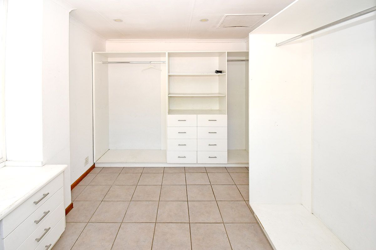 A spacious walk-in dressing room featuring extensive built-in white cabinetry, hanging rails, and tiled flooring.