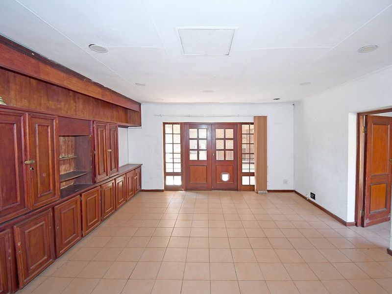 Spacious living area featuring built-in wooden cabinetry, tiled flooring, and direct access to the exterior through timber-framed glass doors.