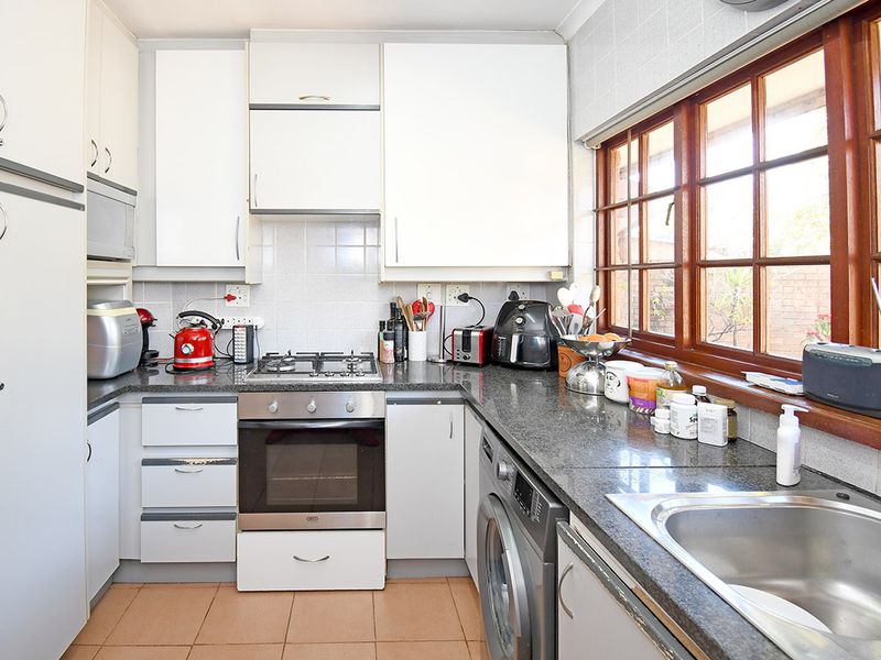 Functional kitchen featuring white cabinetry, granite countertops, built-in oven, gas hob, and integrated laundry plumbing under the counter.