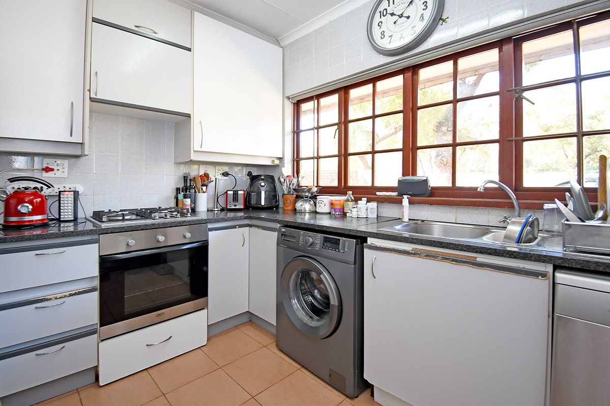 Functional kitchen featuring built-in oven, gas hob, integrated washing machine, stainless steel sink, and ample cabinetry with tiled flooring.