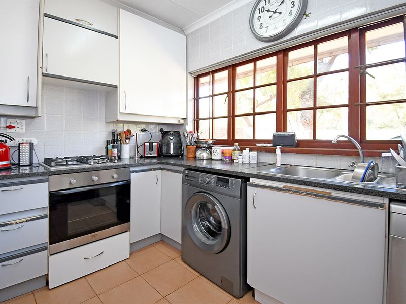 Functional kitchen featuring built-in oven, gas hob, integrated washing machine, stainless steel sink, and ample cabinetry with tiled flooring.