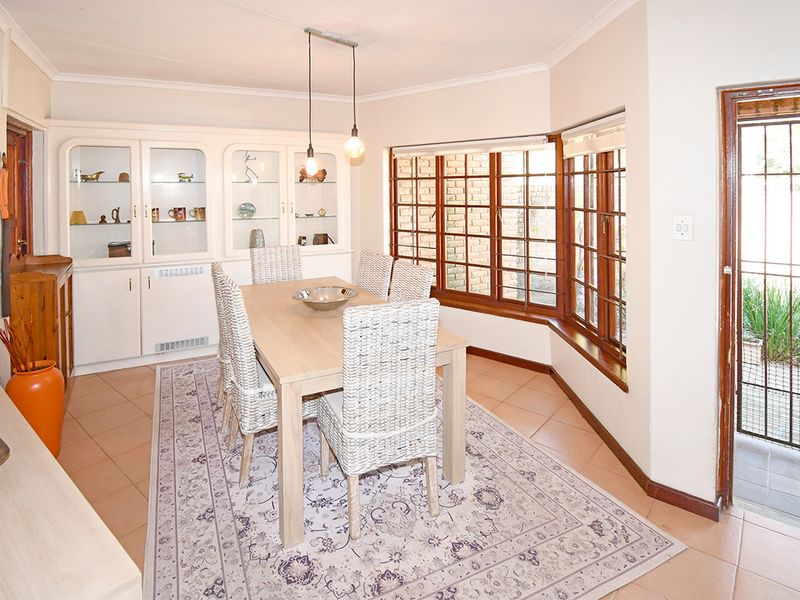 A bright dining room featuring built-in display cabinetry, tiled flooring, and large bay windows with timber frames, providing access to an outdoor area.