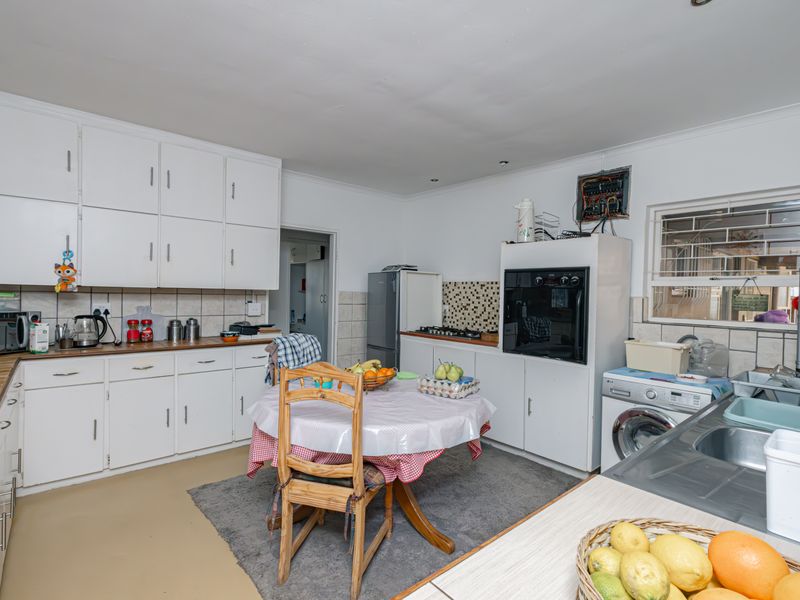 Functional kitchen featuring white cabinetry, built-in oven, hob, and double sink, with an adjacent laundry area and visible electrical distribution board.