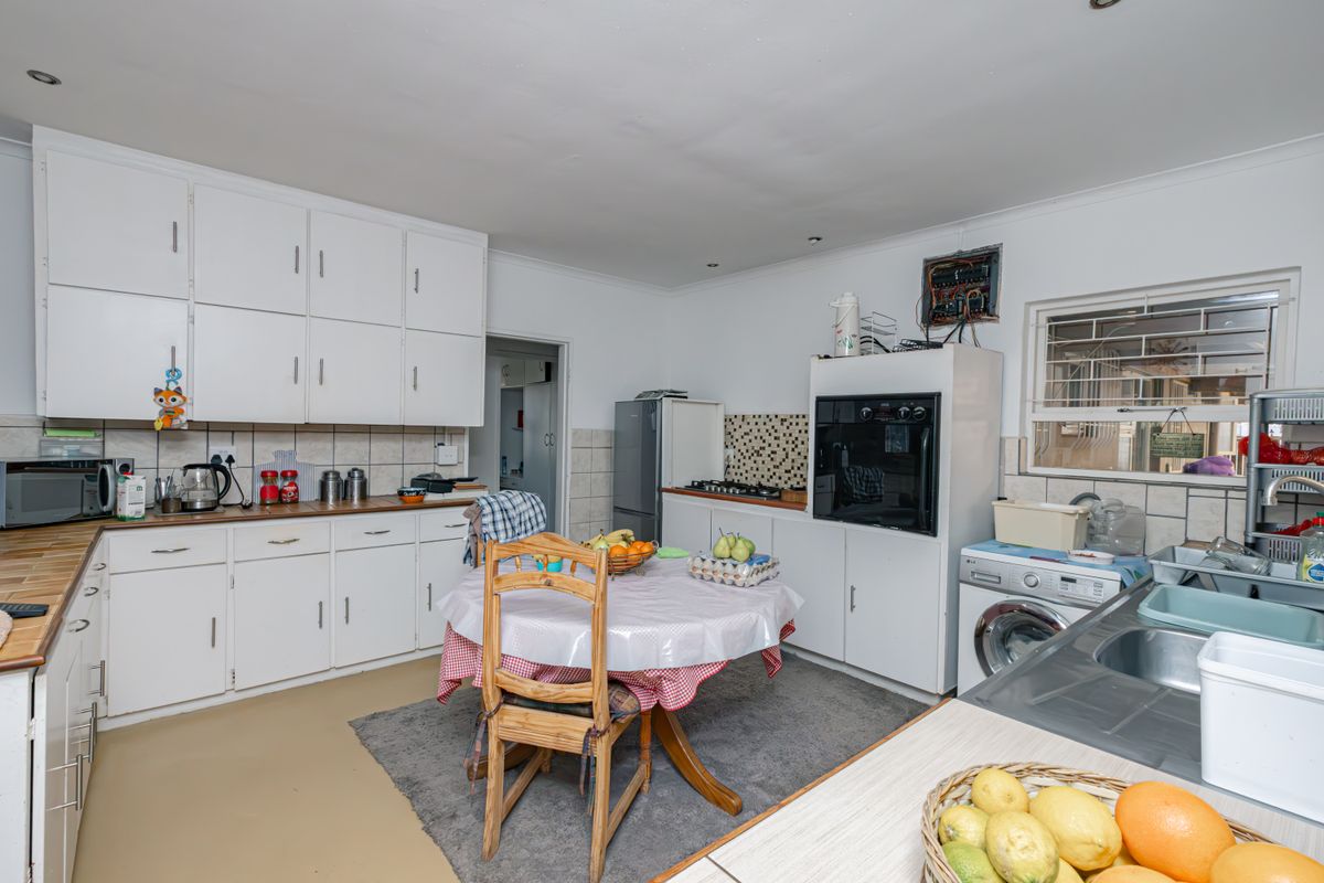 Functional kitchen featuring white cabinetry, built-in oven, hob, and double sink, with an adjacent laundry area and visible electrical distribution board.
