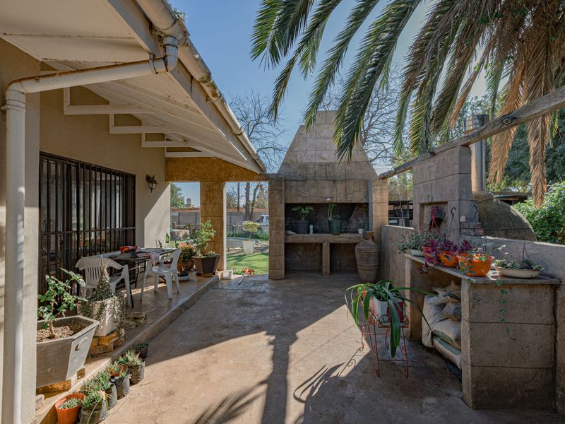 Covered outdoor patio area featuring a built-in stone braai and masonry work, providing a functional space for outdoor entertaining and dining.