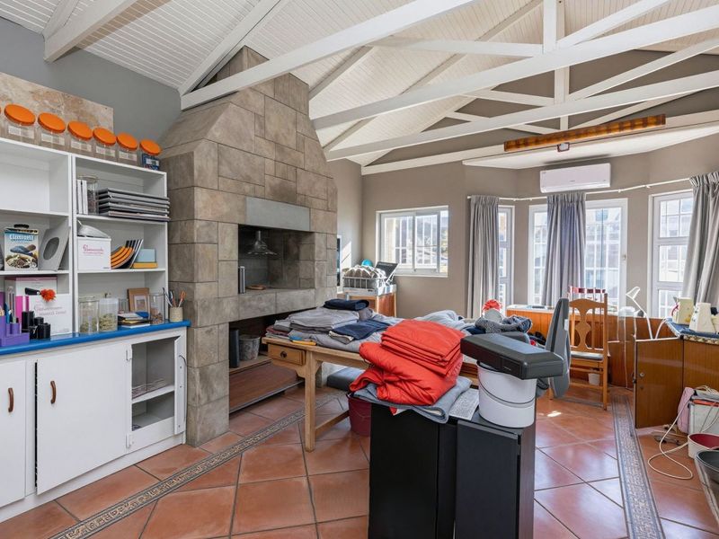 Spacious living area featuring a prominent stone-clad fireplace, exposed beam ceiling, and terracotta flooring, offering a versatile space with built-in storage.