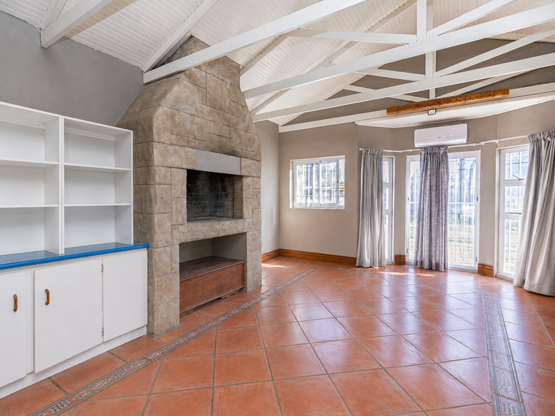 Spacious living area featuring a prominent stone-clad fireplace, exposed white timber trusses, built-in storage cabinetry, and terracotta tiled flooring.