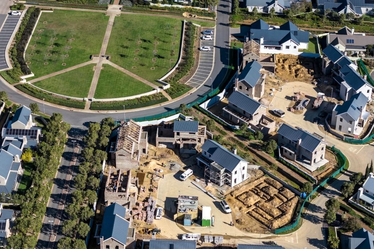 Aerial view of a residential estate under construction, showing multiple housing units in various stages of development alongside established roads and a landscaped park.