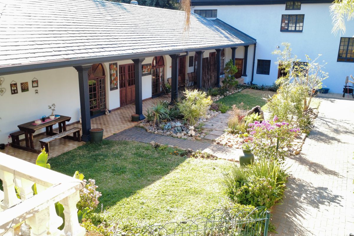 A well-maintained rear courtyard featuring a covered patio with tiled flooring, columns, and a landscaped garden with paved pathways.