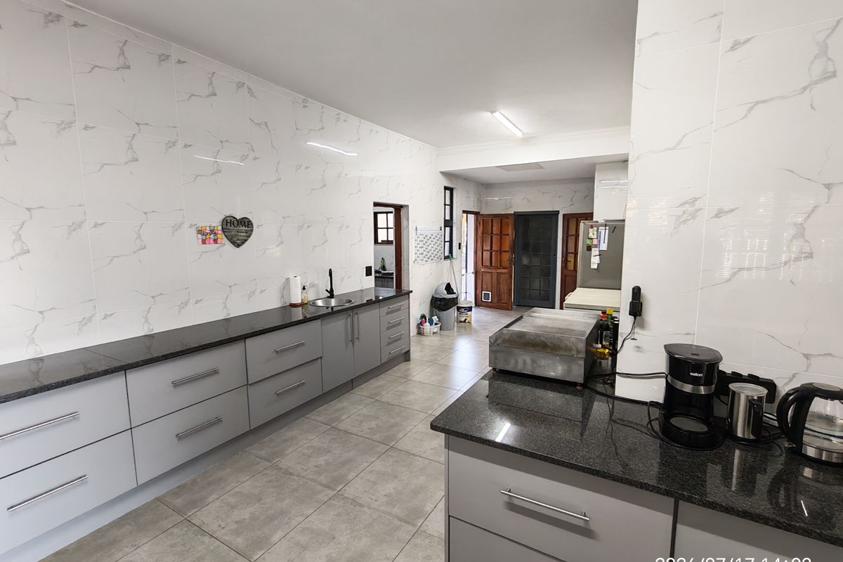A spacious kitchen featuring modern grey cabinetry, granite countertops, and marble-effect wall tiles, providing a clean and functional workspace.