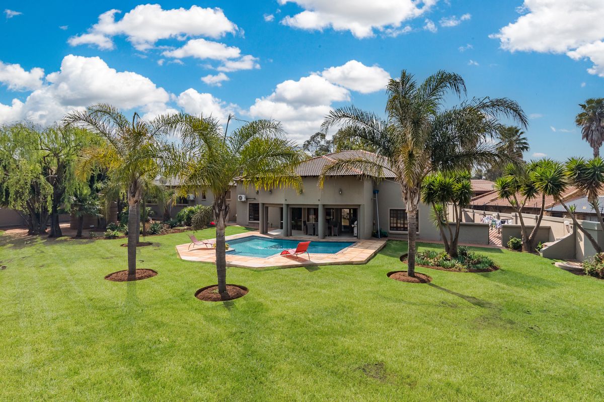 Aerial view of a residential property featuring a well-maintained garden, a swimming pool with a tiled patio, and a spacious rear facade.