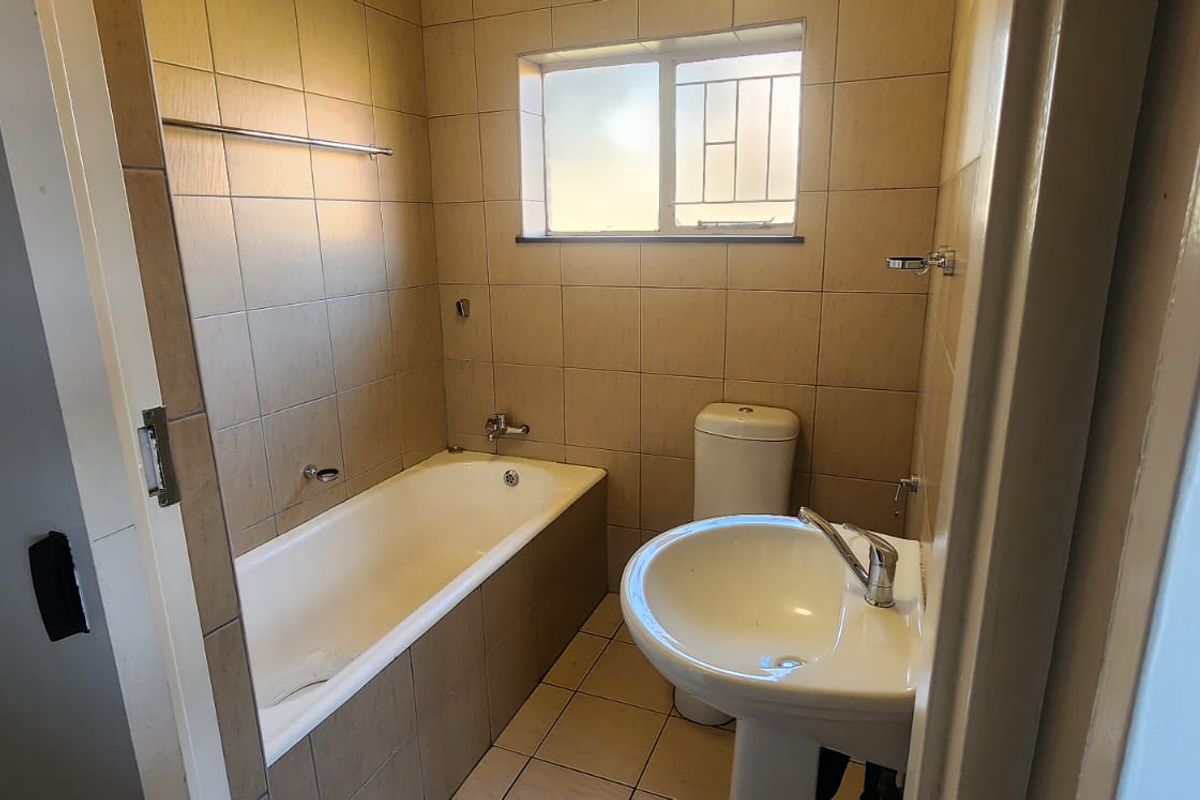 A functional bathroom featuring a bathtub, pedestal basin, and toilet with neutral wall and floor tiling.