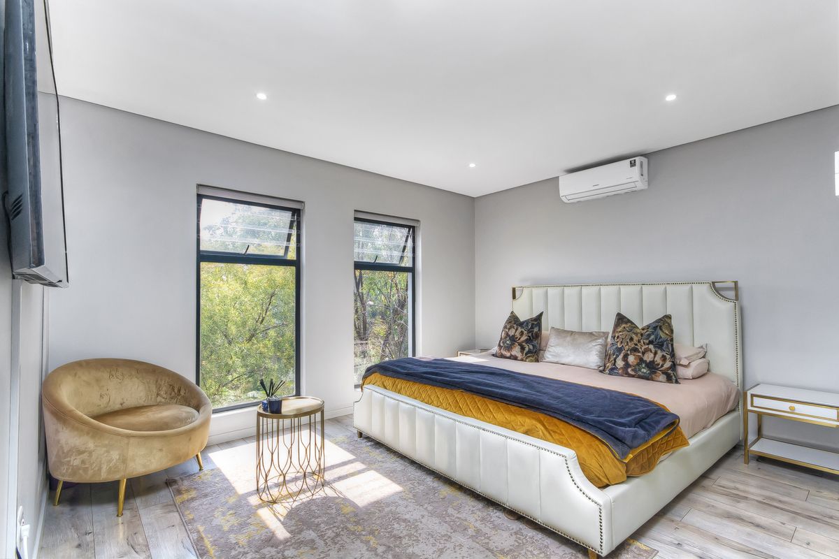 A bright and modern bedroom featuring large windows, recessed ceiling lighting, and a wall-mounted air conditioning unit.