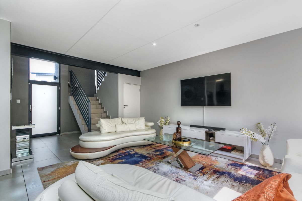 Modern open-plan living area featuring tiled flooring, a sleek staircase with metal railings, and a wall-mounted television setup.