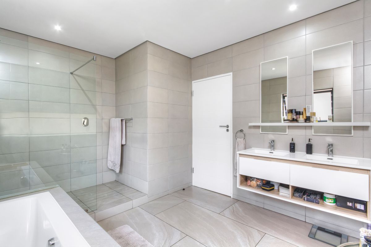 Modern bathroom featuring a double vanity with integrated sinks, a large walk-in glass shower, and neutral floor-to-ceiling tiling.