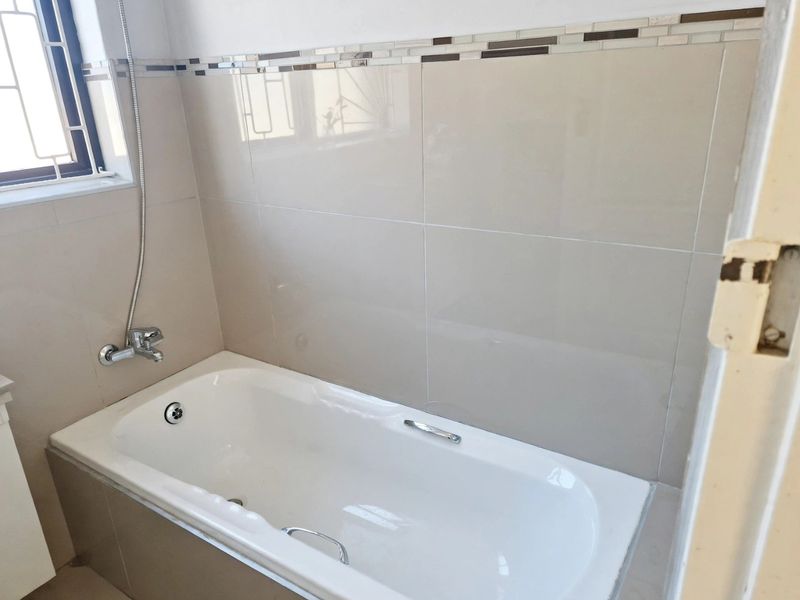 A clean bathroom featuring a built-in bathtub with chrome fixtures and neutral ceramic wall tiling with a decorative mosaic accent border.