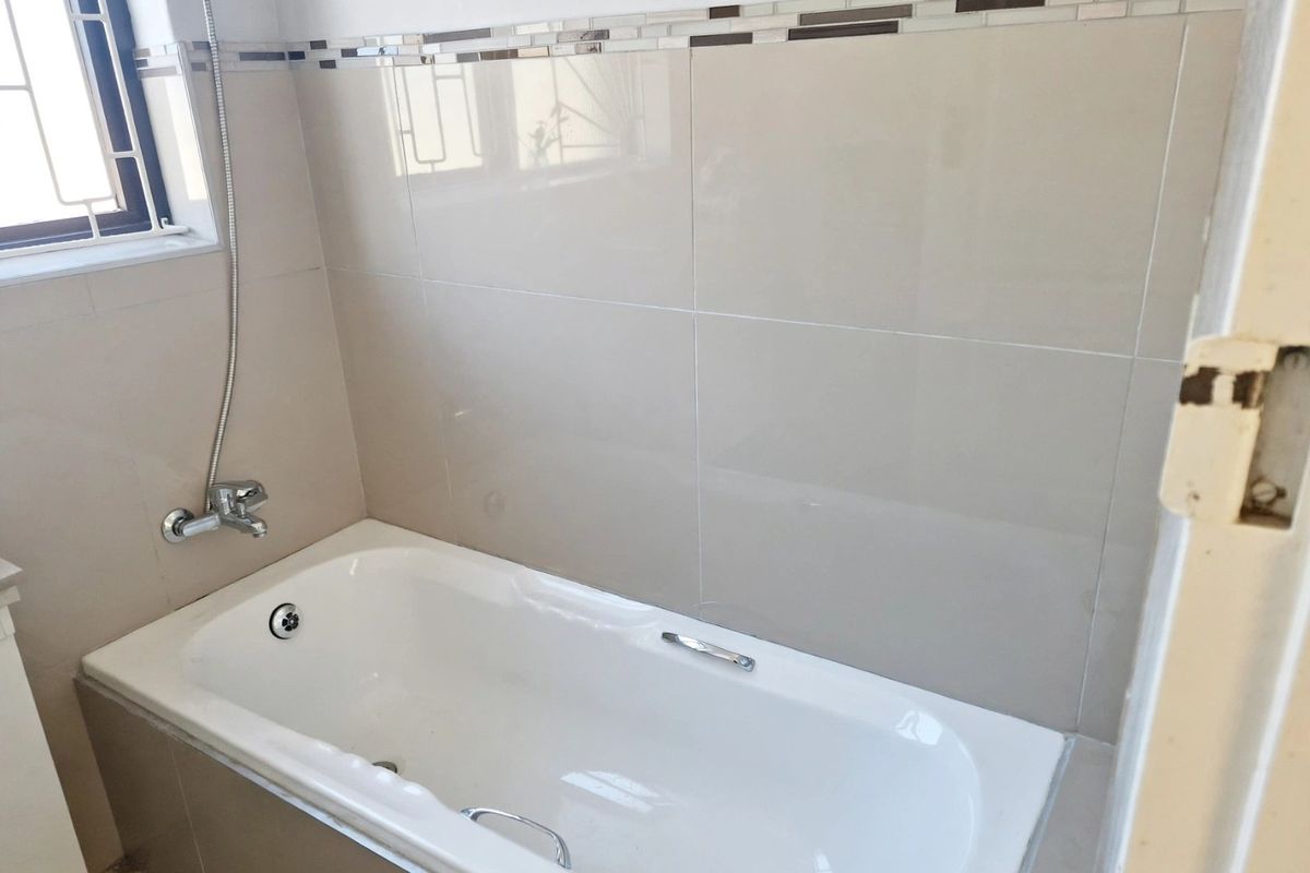 A clean bathroom featuring a built-in bathtub with chrome fixtures and neutral ceramic wall tiling with a decorative mosaic accent border.