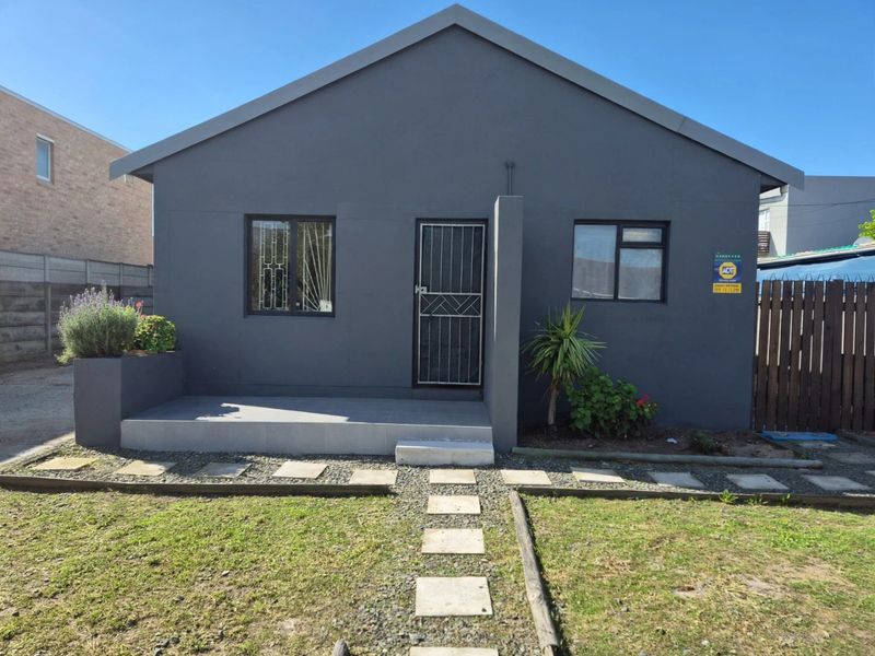 Front elevation of a modern grey-painted house featuring a tiled entrance porch, security gate, and a paved walkway through the front garden.