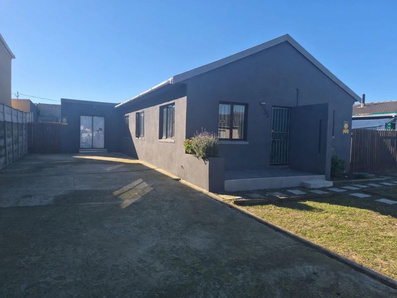 Front elevation of a detached house featuring a dark grey rendered facade, concrete driveway, and security features including bars and a gate.