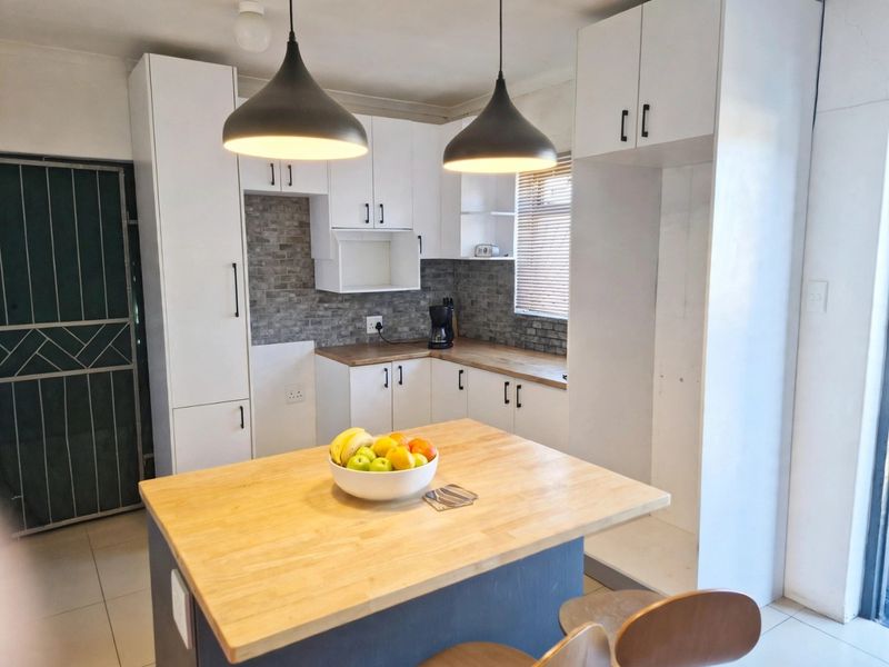 Modern kitchen featuring white cabinetry, wooden countertops, a stone-look tile backsplash, and a central kitchen island with pendant lighting.