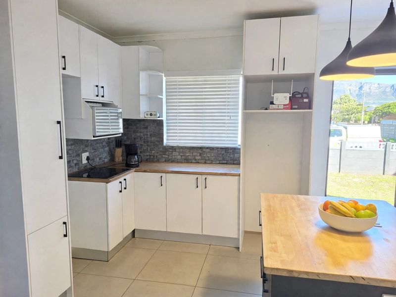 Modern kitchen featuring white cabinetry, timber countertops, a brick-style backsplash, and an electric hob, complemented by tiled flooring and contemporary pendant lighting.
