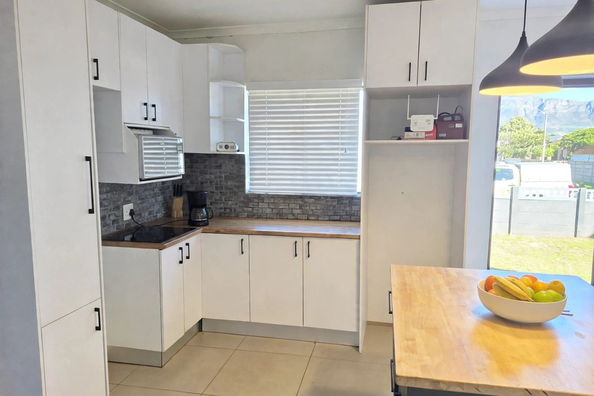 Modern kitchen featuring white cabinetry, timber countertops, a brick-style backsplash, and an electric hob, complemented by tiled flooring and contemporary pendant lighting.