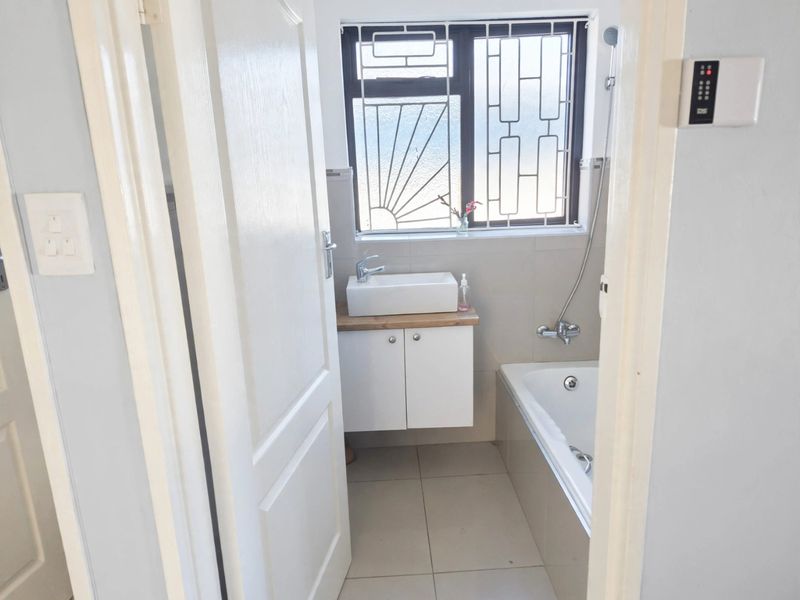 A compact, well-maintained bathroom featuring a modern vessel sink on a vanity cabinet, a bathtub with shower mixer, and tiled finishes.