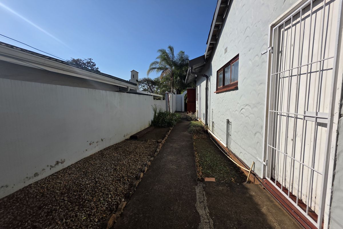 A narrow side passage featuring a concrete walkway, gravel garden bed, and boundary wall, providing access along the side of the property.