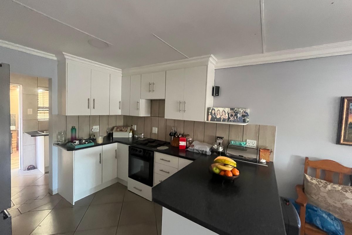 A functional kitchen featuring white cabinetry, dark countertops, a built-in oven, and tiled flooring, with an open layout connecting to adjacent spaces.