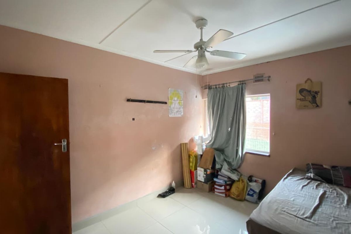 A bedroom featuring tiled flooring, a ceiling fan, and a timber door, currently requiring cosmetic updates to the wall finishes.