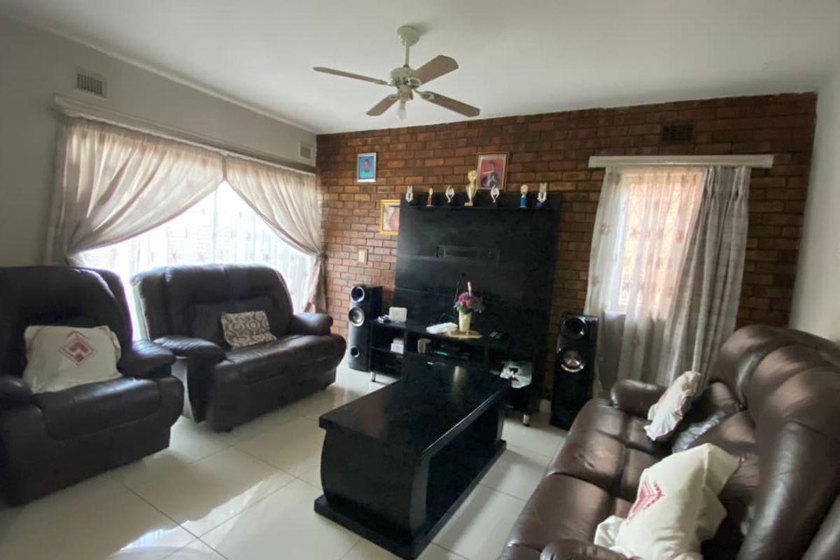 A living room featuring an exposed brick accent wall, tiled flooring, and a ceiling fan, providing a comfortable and functional living space.