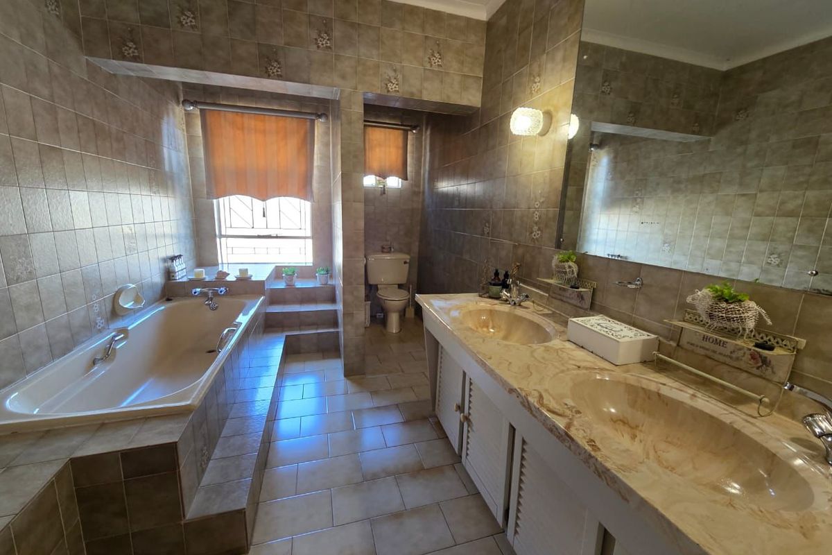 Spacious bathroom featuring a built-in bathtub, double vanity with marble countertop, and full-width mirror, finished with neutral ceramic tiling throughout.