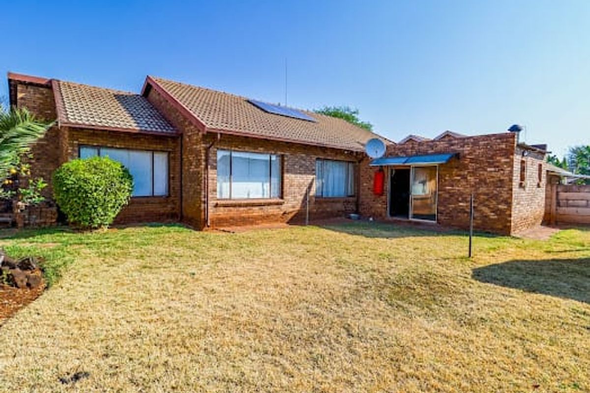 Rear view of a face brick duet property featuring a tiled roof, solar panel, and a private garden area with a sliding door entrance.