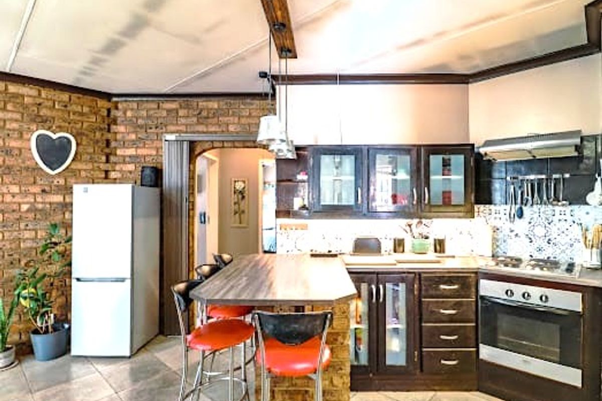 Kitchen featuring exposed brick walls, dark cabinetry, built-in oven, hob, extractor fan, and a breakfast bar with tiled flooring.