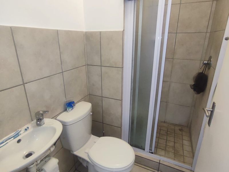 Compact bathroom featuring a shower enclosure, toilet, and wall-mounted basin with neutral tiled finishes throughout.