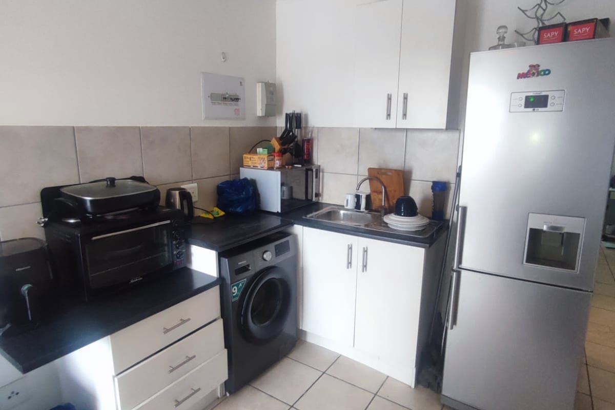 Compact kitchen featuring white cabinetry, dark countertops, tiled backsplash, and dedicated space for laundry appliances, offering a functional layout for an apartment.