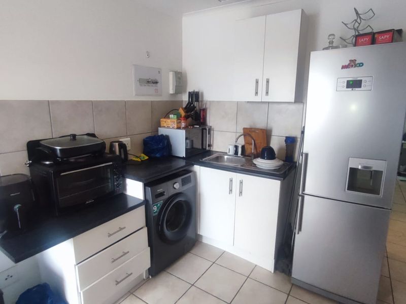 Compact kitchen featuring white cabinetry, dark countertops, tiled backsplash, and dedicated space for laundry appliances, offering a functional layout for an apartment.