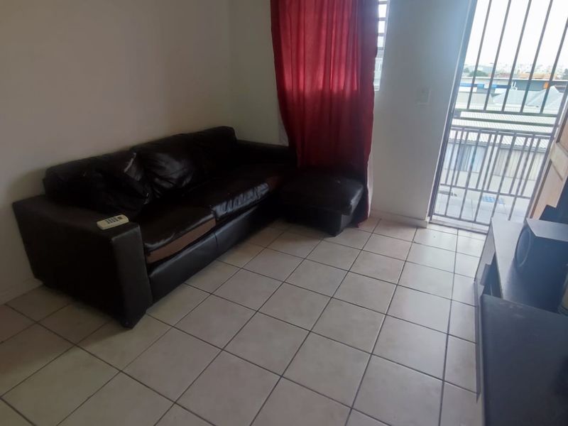 A living room area featuring tiled flooring and a sliding door with a security gate leading to an outdoor space.