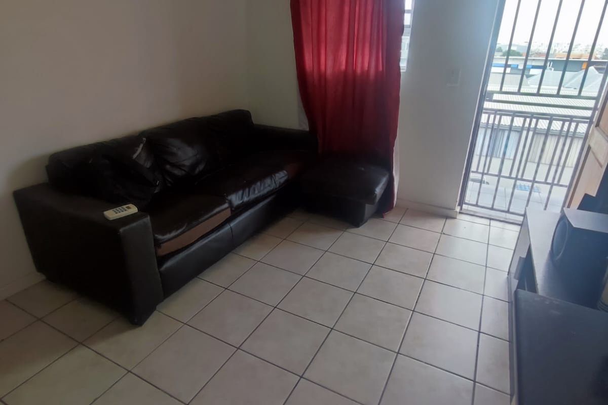 A living room area featuring tiled flooring and a sliding door with a security gate leading to an outdoor space.