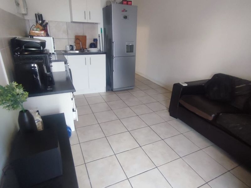 Open-plan living area featuring tiled flooring and a compact kitchen with built-in cabinetry and a tiled backsplash.