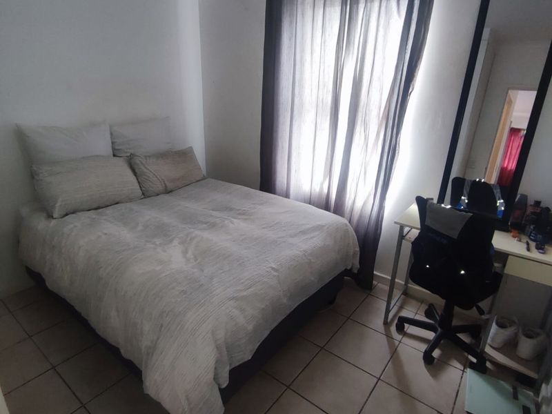 A functional bedroom featuring tiled flooring and a window with curtain rod, providing a neutral space ready for personalization.