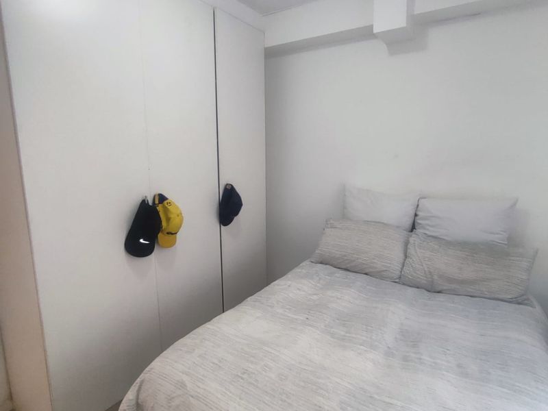 A compact bedroom featuring white built-in wardrobes and tiled flooring, providing a functional and neutral living space.